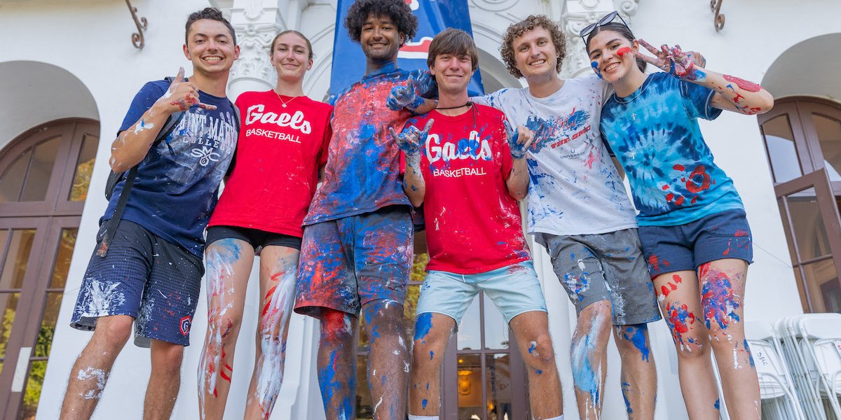 Six students covered in paint in front of the sign GOD IS A GAEL