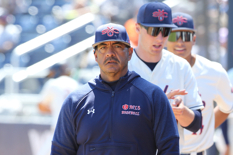 Baseball coach Eric Valenzuela in foreground with two baseball players in background, May 2024