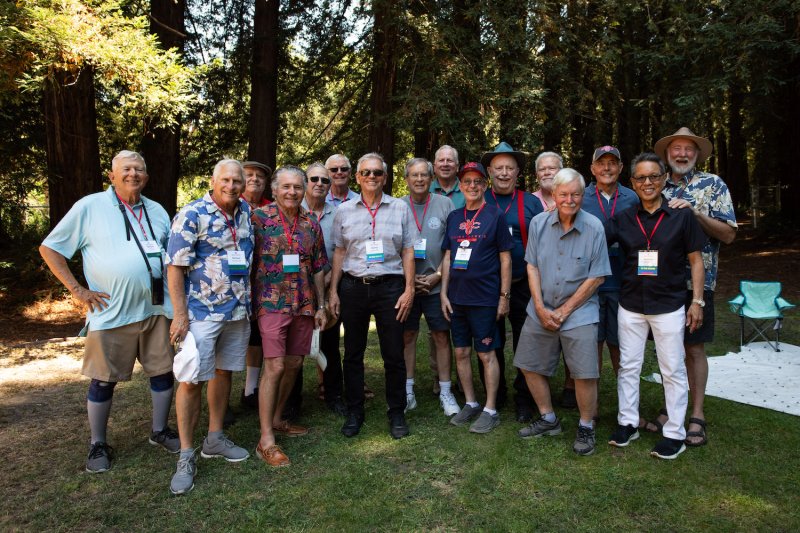 16 members of the class of 1969 smile for a photo under redwood trees at Reunion 2024