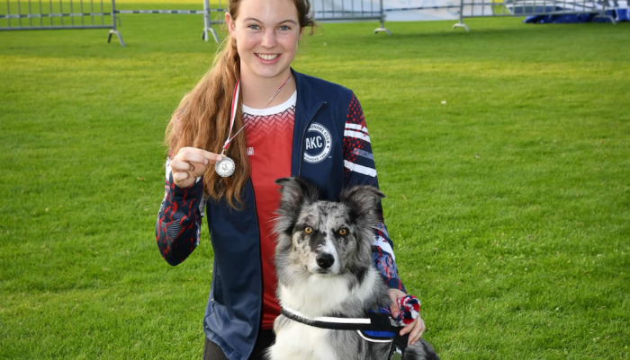 A student holding a medal and posing with her dog