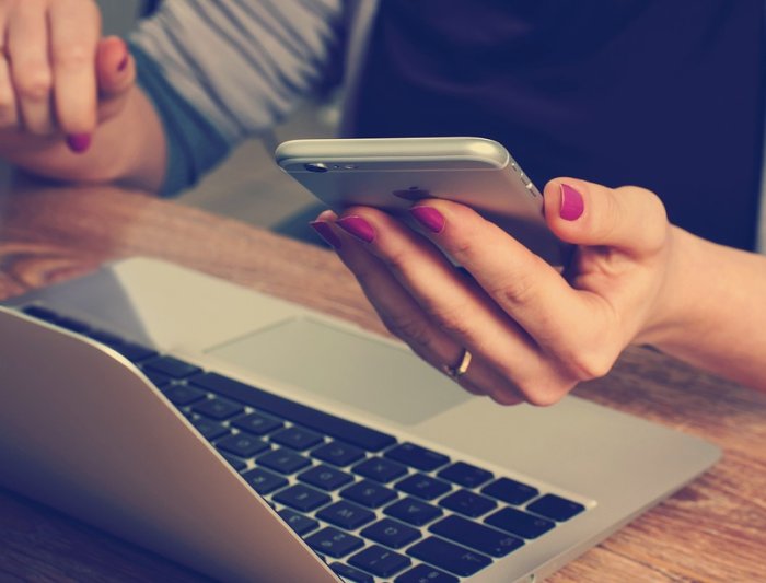 hand holding smartphone over laptop